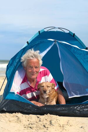Single senior man with his dog camping in shelter at the beachの写真素材