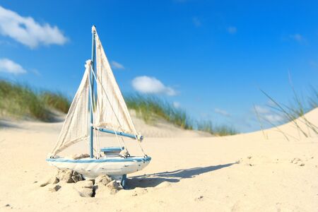 Toy sail boat in the dunes at the beachの写真素材
