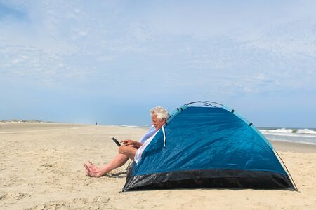 Single senior man with digital tablet camping in shelter at the beachの写真素材