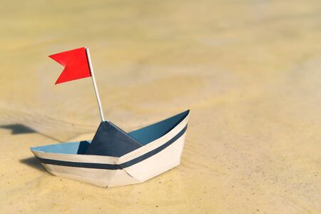 Blue and white paper boat with red flag floating on waterの写真素材