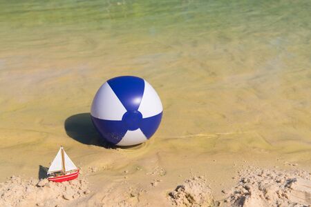 Toy boat and Inflatable blue and white beach ball floating on waterの写真素材