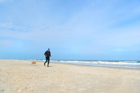 Healthy senior man running with dog at the beach の写真素材