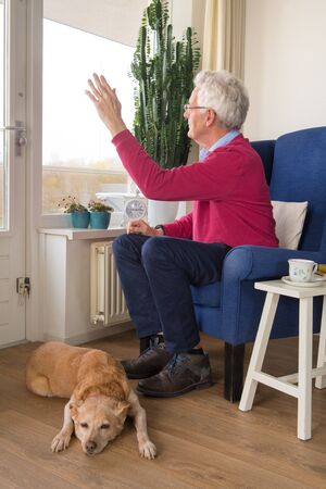 Senior man alone sitting in chair and looking outsideの写真素材