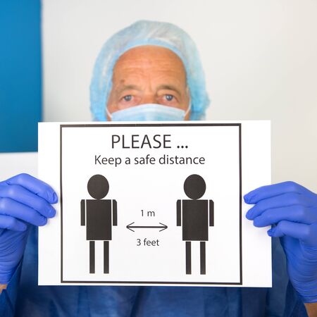 Doctor with face mask and protective clothing is asking for safe distance from 1 meter or 3 feetの写真素材