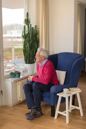 Senior man alone sitting in chair and looking outsideの写真素材