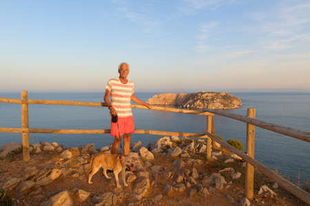 Man with dog in front of landscape with Les Medes islands in sunset at the horizonの写真素材