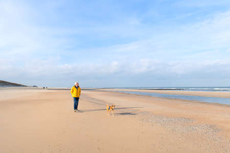 Senior man walking with dog at the Dutch coastの写真素材