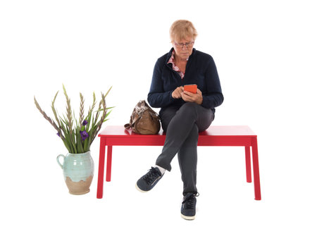 Senior woman with mobile phone is waiting and reading a magazineの写真素材