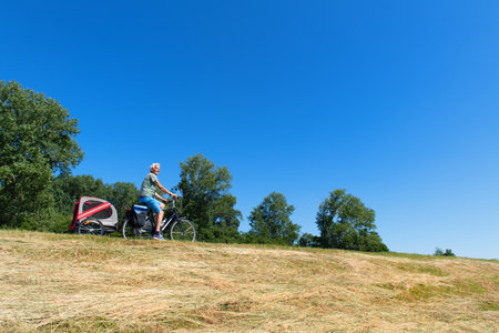 Senior man on bike with dog in a trailer on a Dutch dikeの写真素材