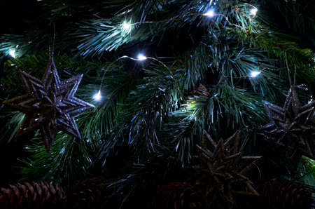 Spruce branches closeup. Silver snowflakes, pines and lighting garland on the spruce branch. Lights on the Christmas tree. Christmas background.の写真素材