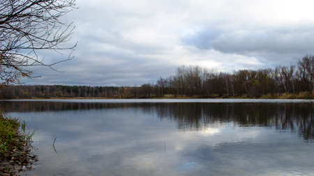 City landscape. Forest and houses around lake. Ripples on water. Stormy weather. Stormy clouds. Sky, sunlight and trees reflecting on water. Houses reflecting in water.の写真素材