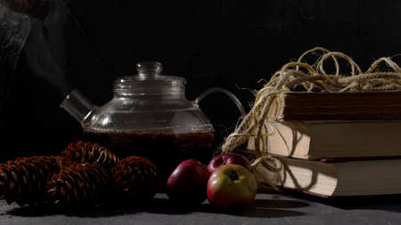 Glass teapot, old books, pine trees and apples on dark gray background.の写真素材