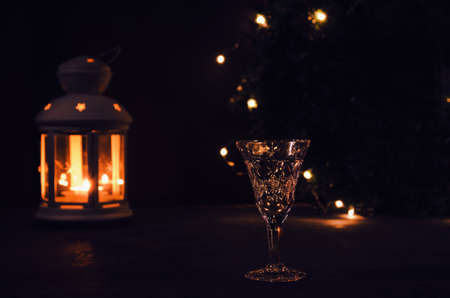 Glass with white wine with garland lights and candle lantern on the background. dark picture. Burning candle. Golden beverage in the glass. Beautiful lights reflected in the glass.の写真素材