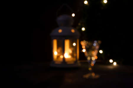 Shiny blurred background for design. Glass with white wine with garland lights and candle lantern blurred. Night picture. Beautiful lights.の写真素材