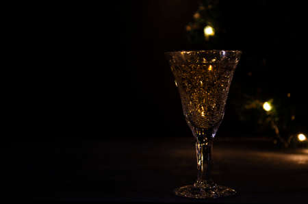 Glass with white wine with garland lights on the background. dark picture. Golden beverage in the glass. Beautiful lights reflected in the glass.の写真素材