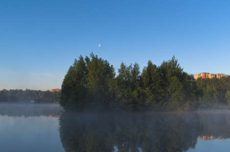 bright blue sky. Trees near water. Tree reflection on water surface. transparent mist. nature background.の写真素材