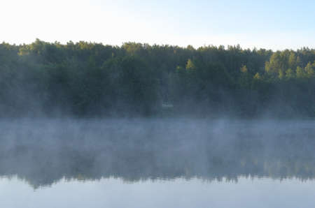 Transparent mist cover the water. Forest near the lake reflected in water. early morning. bright sunny sky. clear transparent air. nature background.の写真素材