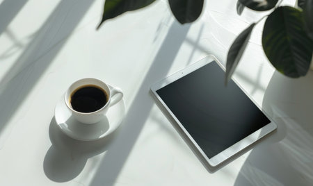 Tablet on a light gray table with a cup of tea on the left, sunlight from windowの素材