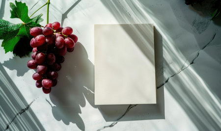 Closed notebook on a white table with a bunch of grapesの素材