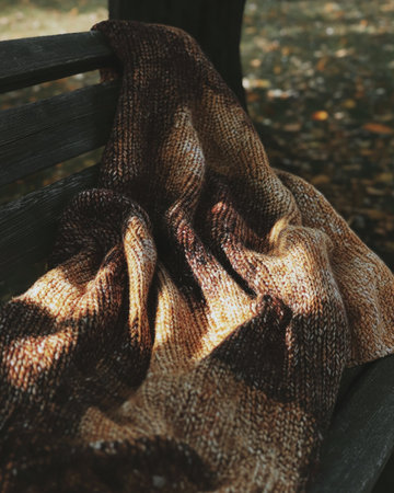 Knitted autumn blanket, rich earthy tones, draped on a benchの素材