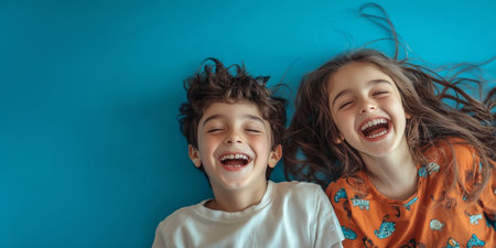 A happy boy and girl smiles against a soft blue background. Little kids take a photo for an advertisement of children's clothing. An image for dental concepts, childhood happiness, and family themesの素材