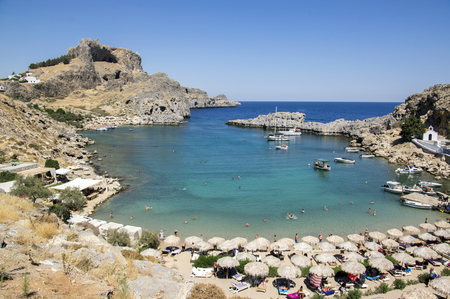 Lindos, Rhodes / GREECE - 7 September, 2018: One of the most amazing beaches on Rhodes with boats, sunbeds, sun umbrellas and visitors during summer season with great view to Acropolisのeditorial素材