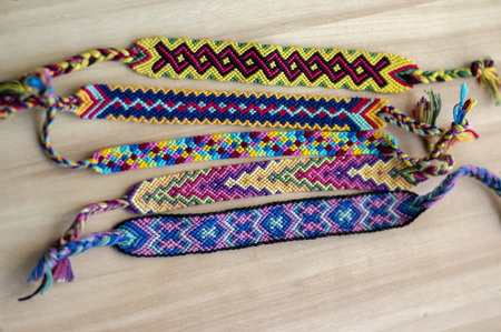 Five handmade homemade colorful natural woven bracelets of friendship on wooden board, group of...