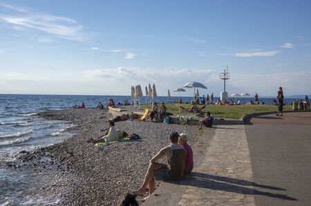 Izola / SLOVENIA - June 23, 2018: People enjoying great summer day on stone beach. Sunlight and blue sky.のeditorial素材