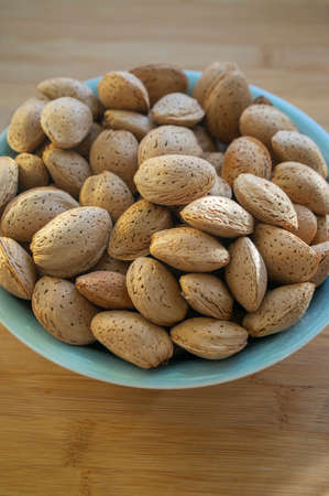 Almonds on table in hard nutshells, group of dry ripened fruits in blue bowl, harvested healthy food...