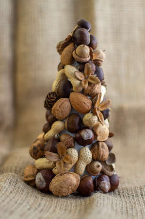 Christmas tree made of autumn ripened brown fruits on jute beige background, diy craft products chestnuts cones beech nuts nuts almonds walnuts peanuts marrons acornsの写真素材