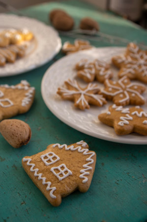 Painted traditional Christmas gingerbreads arranged on white plates on old vintage painted table in daylight, various xmas shapes trees, houses and snowflakesの写真素材