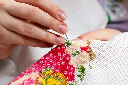Woman hands doing cross-stitch. A close up of  embroidery.