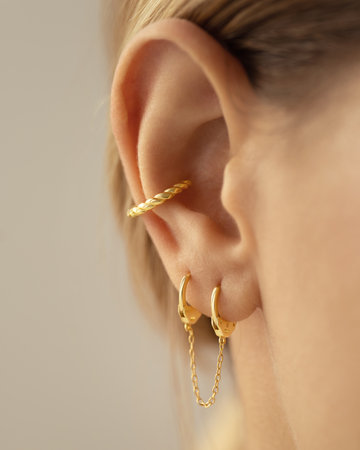 Woman's ear with gold earrings in the shape of handcuffs, close-up view