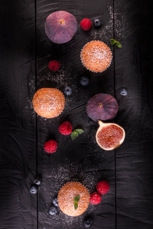 Tasty muffins on a black wooden table with fruits, raspberries, blueberries and figs. Top Viewの写真素材