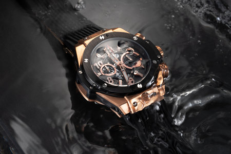 A beautiful gold luxury men's watch with a black strap on a beautiful black background with...