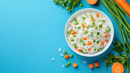 A vibrant bowl of rice mixed with green peas and diced carrots sits on a bright blue background. Fresh carrots and herbs surround the bowl, enhancing the inviting presentationの素材