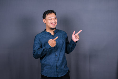 Young asian man isolated on gray background pointing to the side to present a productの写真素材