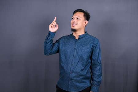 Young asian man isolated on gray background pointing to the side to present a productの写真素材