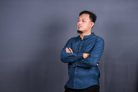 Smiling Asian man with blue shirt standing with hands folded isolated on grey background. Concept of engineering jobsの写真素材