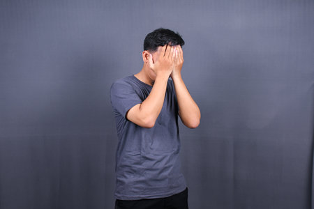 Depressed Asian Young man having stressful time with hands covering face. isolated on gray background.の写真素材