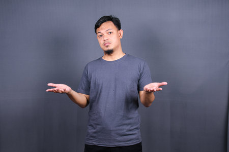 Closeup portrait of clueless funny looking young asian man, arms out asking what do I do now or gesturing I don't know, isolated on gray background.の写真素材
