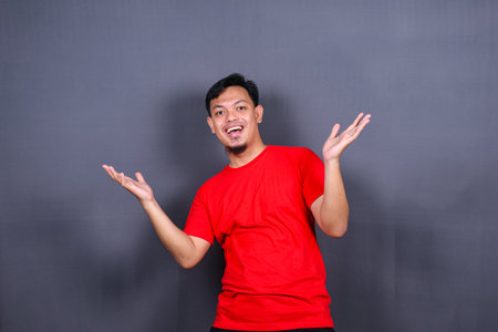 Portrait of an excited asian man standing with raised hands and looking at camera isolated on gray background celebrating succes, victory.の写真素材