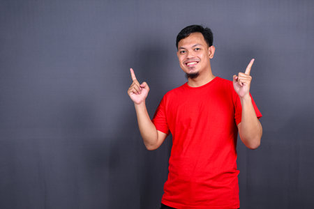 Asian young man in red t-shirt pointing with his finger isolated on gray backgroundの写真素材