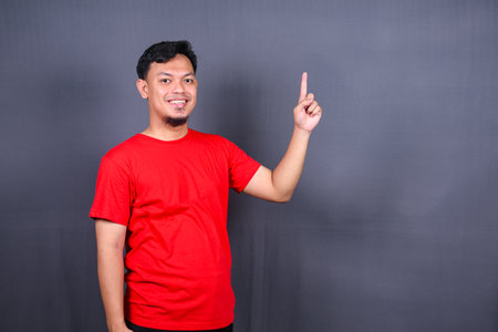 Asian young man in red t-shirt pointing with his finger isolated on gray backgroundの写真素材