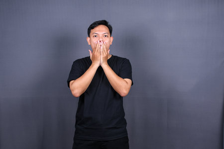 Amazed excited young asian man looking at camera with wow face expression feeling surprised advertising shopping promotion, unbelievable win standing isolated on gray background.の写真素材