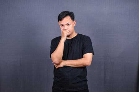 Asian young man thinking about things or idea wearing black t-shirt. Isolated gray backgroundの写真素材