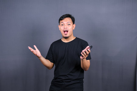 Amazed excited young asian man looking at camera with wow face expression feeling surprised advertising shopping promotion, unbelievable win standing isolated on gray background.の写真素材