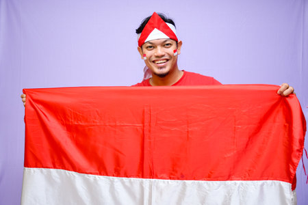 a Man celebrate indonesian independence day on 17 August holding a indonesian flag wearing red shirt and one hand on his chest. isolated over purple backgroundの写真素材