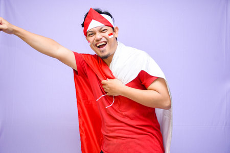 a Man celebrate indonesian independence day on 17 August holding a indonesian flag wearing red shirt and one hand on his chest. isolated over purple backgroundの写真素材