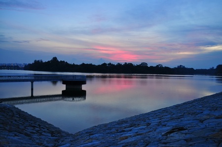 Sunset view with slight red sky of Punggol reservoir, with stones as foregroundの写真素材